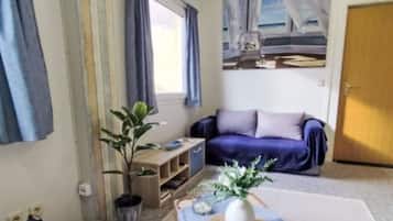 A living room with a sofa, a small table, a potted plant, and a wall-mounted TV.