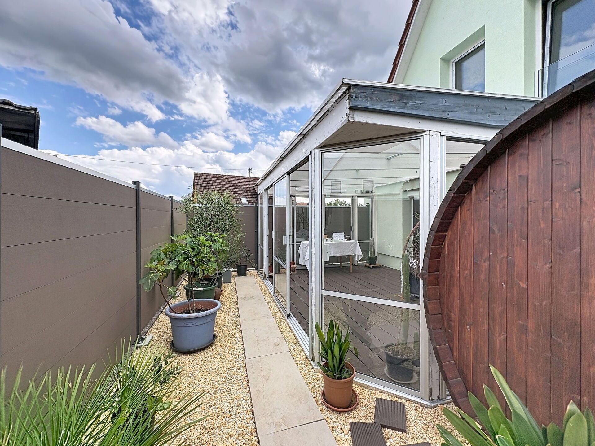A modern patio with a glass enclosure, a wooden fence, and potted plants.