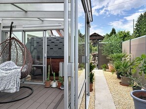 Eine moderne Terrasse mit Hängesessel, Blumentöpfen und Blick auf ein Holzhaus im Hintergrund.