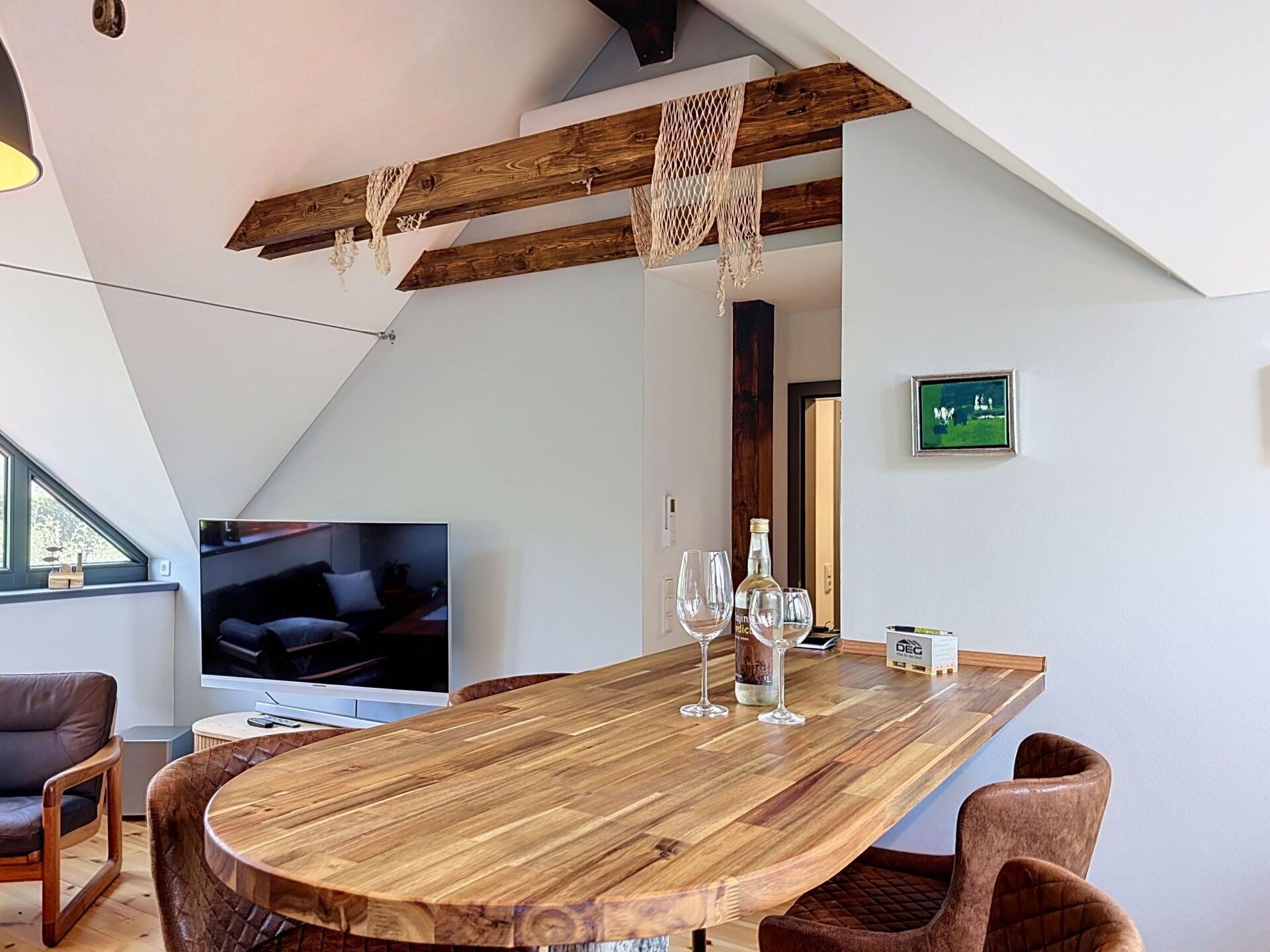 Ein moderner Essbereich mit einem Holztisch, Stühlen und einem Fernseher im Hintergrund.