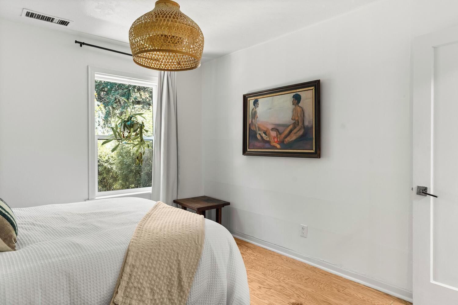 Een slaapkamer met een bed, een raam met gordijnen, een schilderij aan de muur en een hanglamp.
