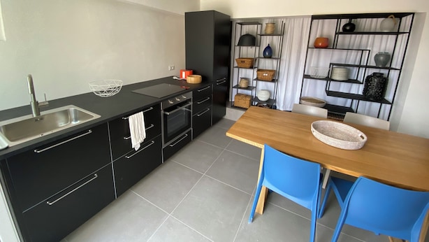 Una cocina moderna con armarios negros, una mesa de comedor de madera y sillas azules.