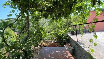 Uma área externa com mesas e cadeiras, cercada por vegetação e um muro de pedra.