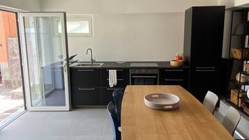 A modern kitchen with a dining area, featuring a wooden table, chairs, a black cabinet, and a sliding glass door leading to an outdoor area.