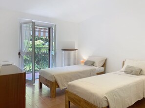 Ein Schlafzimmer mit zwei Betten, einem Holztisch und Blick ins Grüne durch eine Glastür.