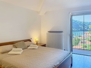 Ein Hotelzimmer mit einem Bett, einem Nachttisch, einer Lampe und einem Fenster mit Blick auf eine Küstenlandschaft.