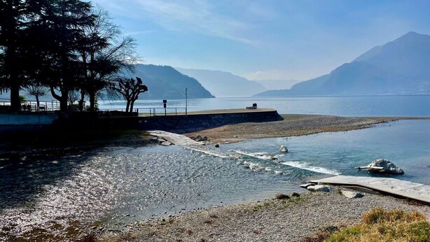 En vacker utsikt över sjön med en stenig strand, en utkiksplattform och berg i fjärran.