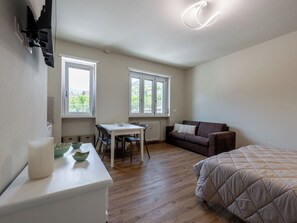 Une pièce de taille modeste comprenant un lit, un canapé, une table à manger avec des chaises et deux fenêtres.