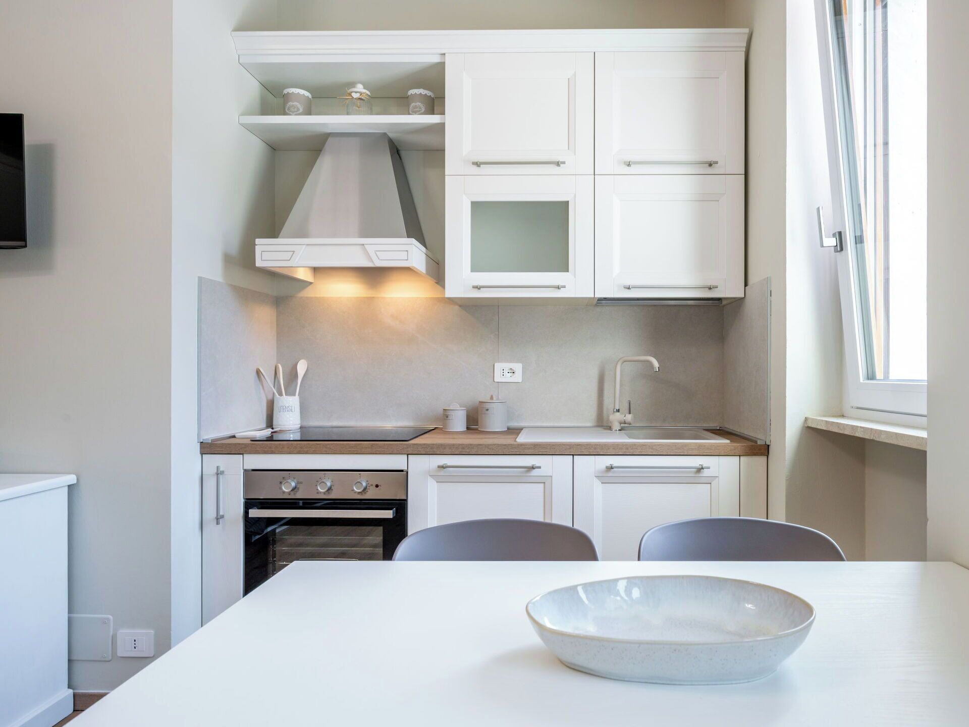 A modern kitchen with white cabinets, a stove, and a dining area with a bowl on the table.