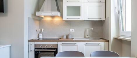 A modern kitchen with white cabinets, a stove, and a dining area with a bowl on the table.