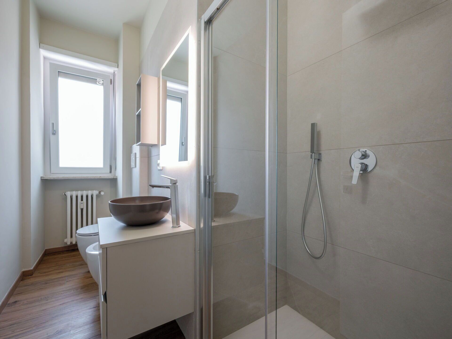 Ein modernes Badezimmer mit einer Duschkabine aus Glas, einem weißen Waschbecken mit Schüssel und einem Spiegel darüber.