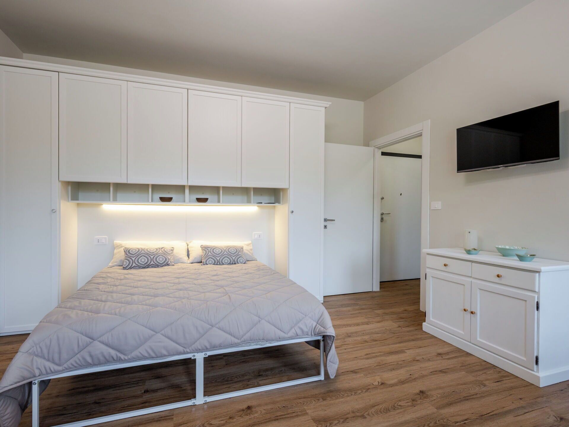 A bedroom with a bed, a wardrobe, a television, and a door.