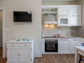 Une cuisine compacte avec des meubles blancs, un four encastré, un four à micro-ondes et un téléviseur à écran plat fixé au mur.