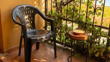 Une chaise en plastique noire, posée sur un sol carrelé, à côté d’une clôture en fer forgé ornée de plantes grimpantes.