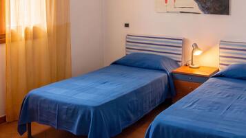 Une chambre avec deux lits, une table de chevet avec une lampe, un tableau au mur et une fenêtre avec des rideaux.