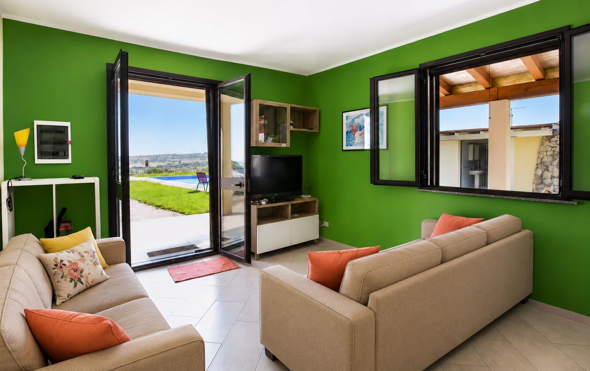 Ein Wohnzimmer mit einer Couch, einem Fernseher und Blick auf einen Swimmingpool.