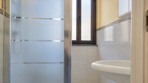 Et badeværelse med et glasbadeværelse, et hvidt badekar og flisegulve.