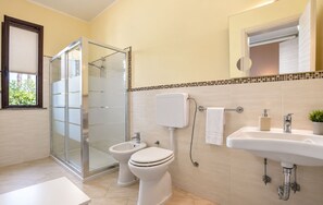 Ein Badezimmer mit Glasdusche, zwei Toiletten, einem Waschbecken und einem Spiegel.