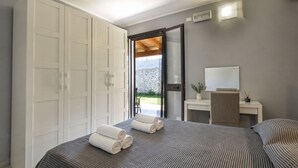 Et soveværelse med seng, garderobe, badeværelsesspejl, et natbord med en vase og udsigt udad.