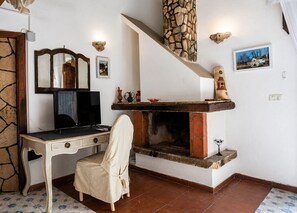 Ein Zimmer mit Kamin, Schreibtisch, Sessel, Fernseher und einer Treppe.