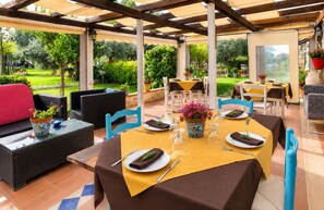 Eine Terrasse im Freien mit Tischen und Stühlen, umgeben von viel Grün.