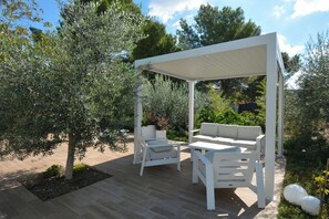 Eine Terrass mit einem weißen Pergola, zwei weißen Sofas und einem kleinen Tisch.