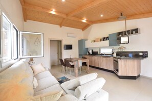 Ein modernes Wohnzimmer mit einer Couch, einem Esstisch und einer Küchenzeile mit Herd und Schränken.