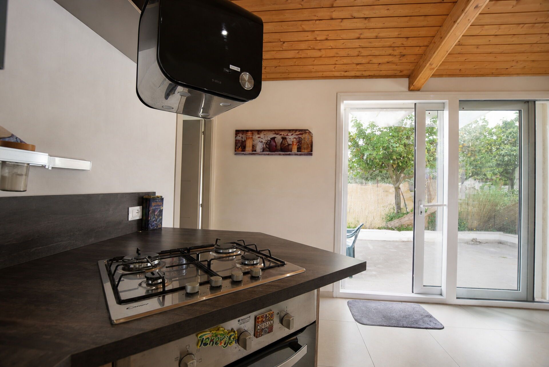 Una cocina moderna con estufa a gas, techo de madera y vistas al exterior a través de un ventanal.