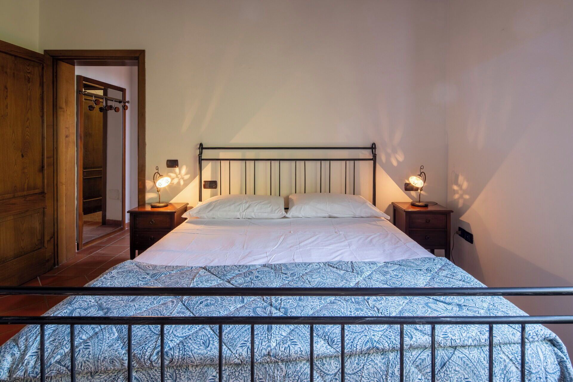 Ein Schlafzimmer mit einem Bett, zwei Nachttischen mit Lampen, einem Holzschrank und einem Metallbettgestell.
