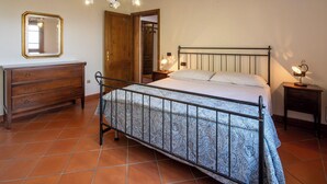 Um quarto com cama, cômoda, espelho e uma porta que dá para outro ambiente.