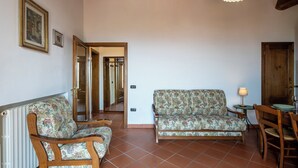 Uma sala de estar com dois sofás de madeira, uma mesa de jantar com cadeiras e uma porta que dá para outro quarto.