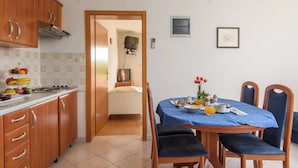 A compact kitchen with a dining area, a small TV mounted on the wall, and a framed picture on the wall. - A1 – apartment Robi with shared heated pool & balcony, near the beach (Seget Vranjica)