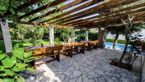 An outdoor patio with stone flooring, wooden benches, and a pergola structure. - A1 – apartment Robi with shared heated pool & balcony, near the beach (Seget Vranjica)