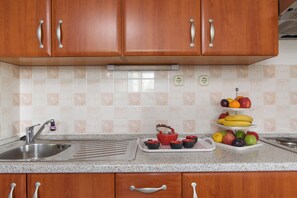 A kitchen with wooden cabinets, a stainless steel sink, a granite countertop, and a fruit display. - A1 – apartment Robi with shared heated pool & balcony, near the beach (Seget Vranjica)