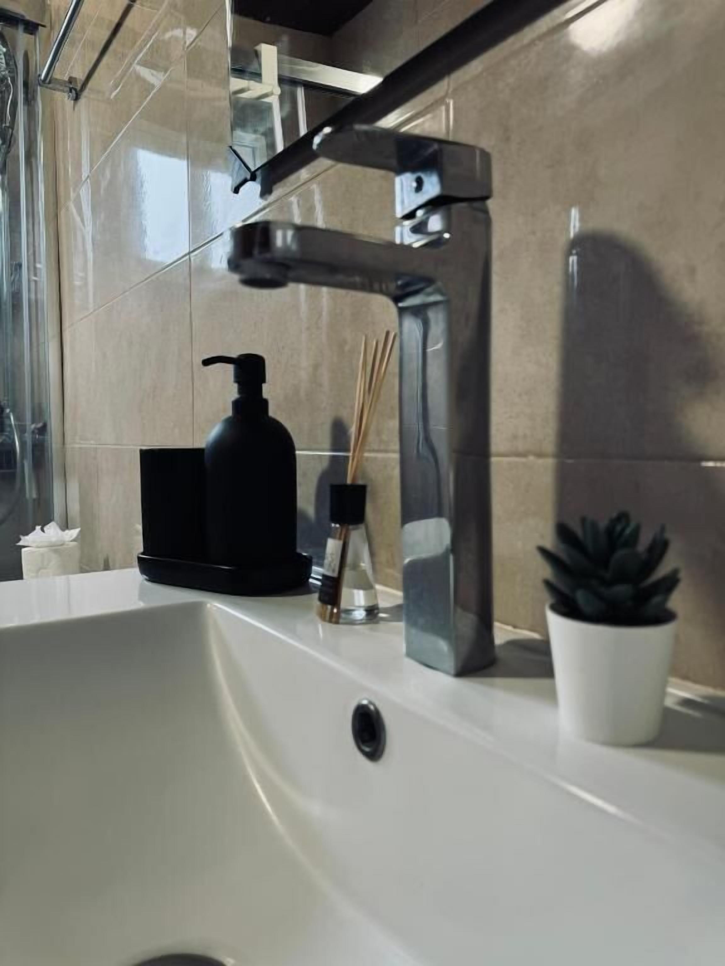 Un lavamanos de baño con una llave moderna, un dispensador de jabón y una planta en maceta.