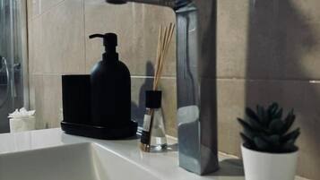 Un lavamanos de baño con una llave moderna, un dispensador de jabón y una planta en maceta.