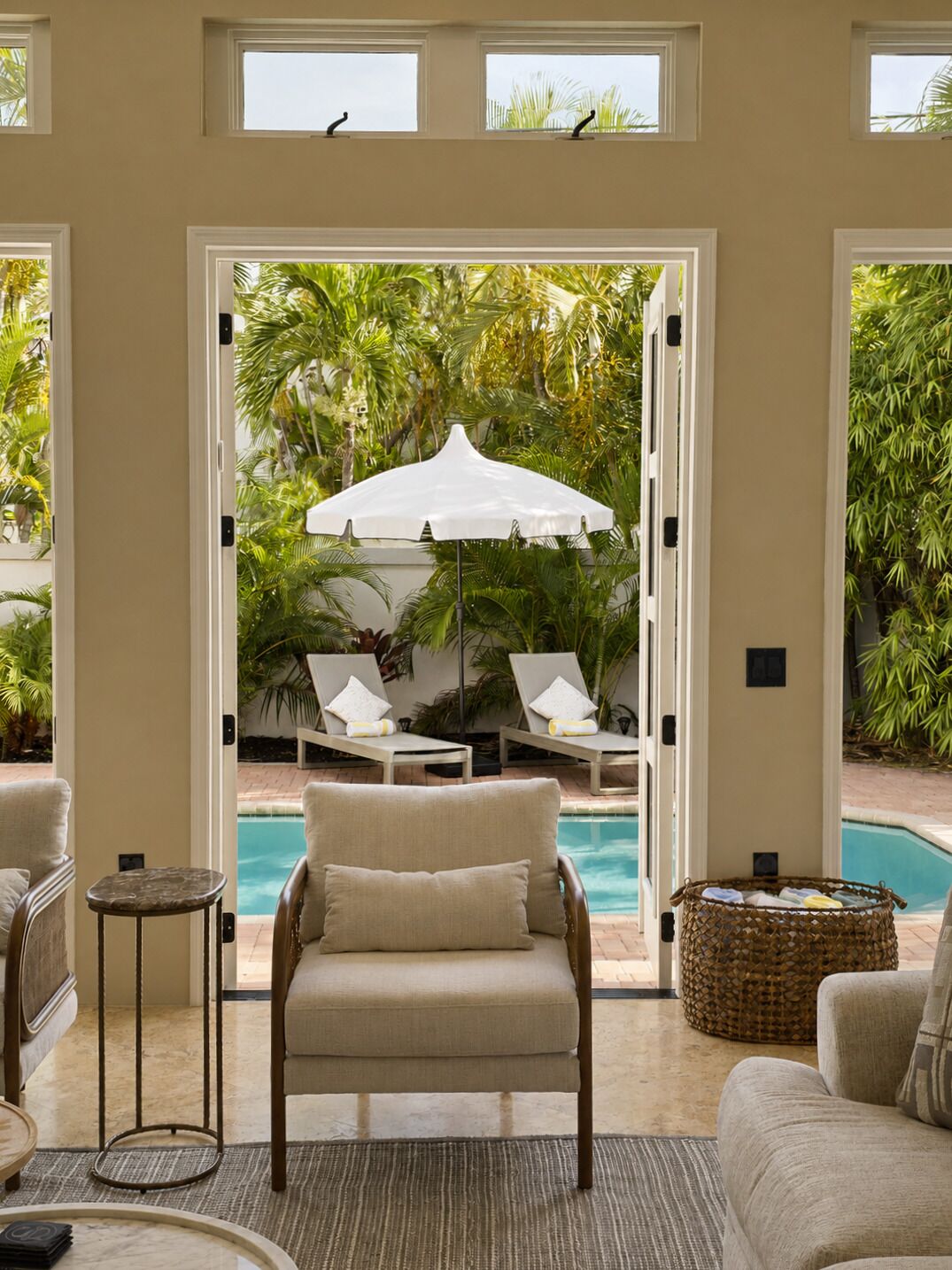 Una habitación con vista a una piscina, una silla, una mesita y una cesta de mimbre.