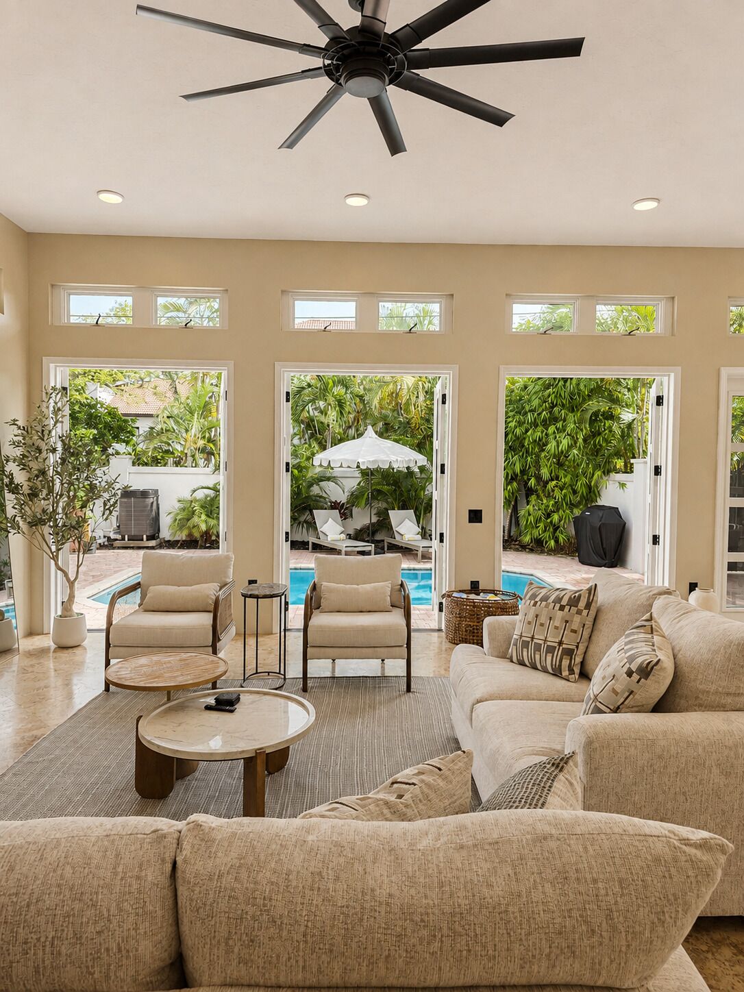 A spacious living room with a ceiling fan, large windows, and a view of a swimming pool.