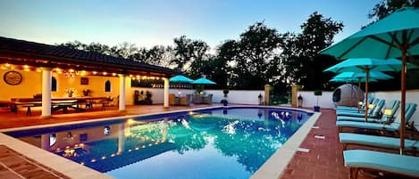 A swimming pool with lounge chairs and umbrellas, surrounded by a patio area with tables and chairs.