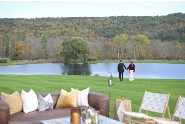 Vista de un lago con una zona verde, una terraza de madera y el lago.