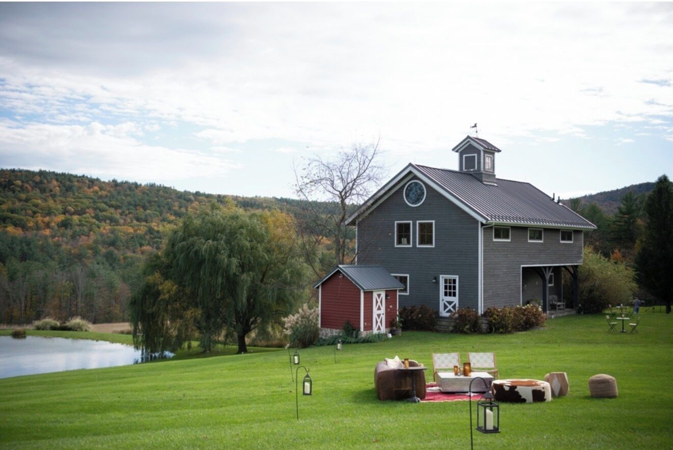 A large house with a barn, a grassy lawn, and a lake in the background.