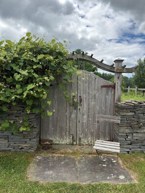 A rustic wooden gate with a stone wall, a bench, and a cloudy sky.