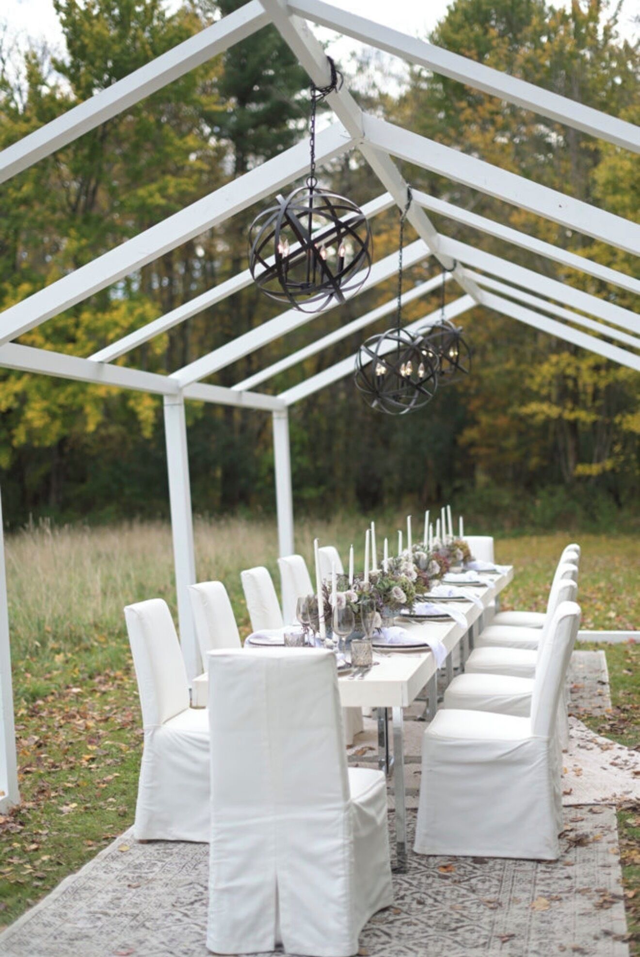 Un espace extérieur abrité, aménagé pour les repas, avec des chaises et des tables blanches, le tout intégré dans un décor naturel.