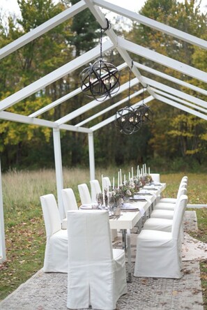 Un espacio comedor al aire libre cubierto con sillas y mesas blancas, frente a un paisaje natural.