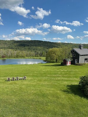 A grassy area with a pond, a red barn, and a house with a metal roof.