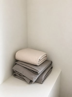 A stack of folded blankets on a white shelf against a plain wall. - Chic Studio Near Downtown, Hospitals & Stadiums (Detroit)