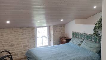 A bedroom with a sloped ceiling, a bed with patterned bedding, a nightstand, and a window.