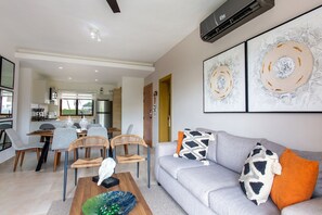 Ein modernes Wohnzimmer mit grauem Sofa, einem Couchtisch und einem Essbereich mit Stühlen und einem Tisch.