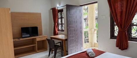A hotel room with a bed, a desk, a television, and a window with curtains.