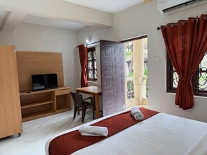 A hotel room with a bed, a desk, a television, and a window with curtains. - White Rose By The Beach (Baga)